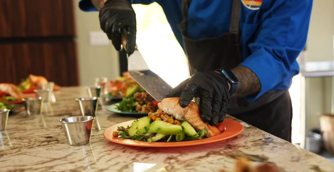 Sliced grilled protein being plated over a fresh salad