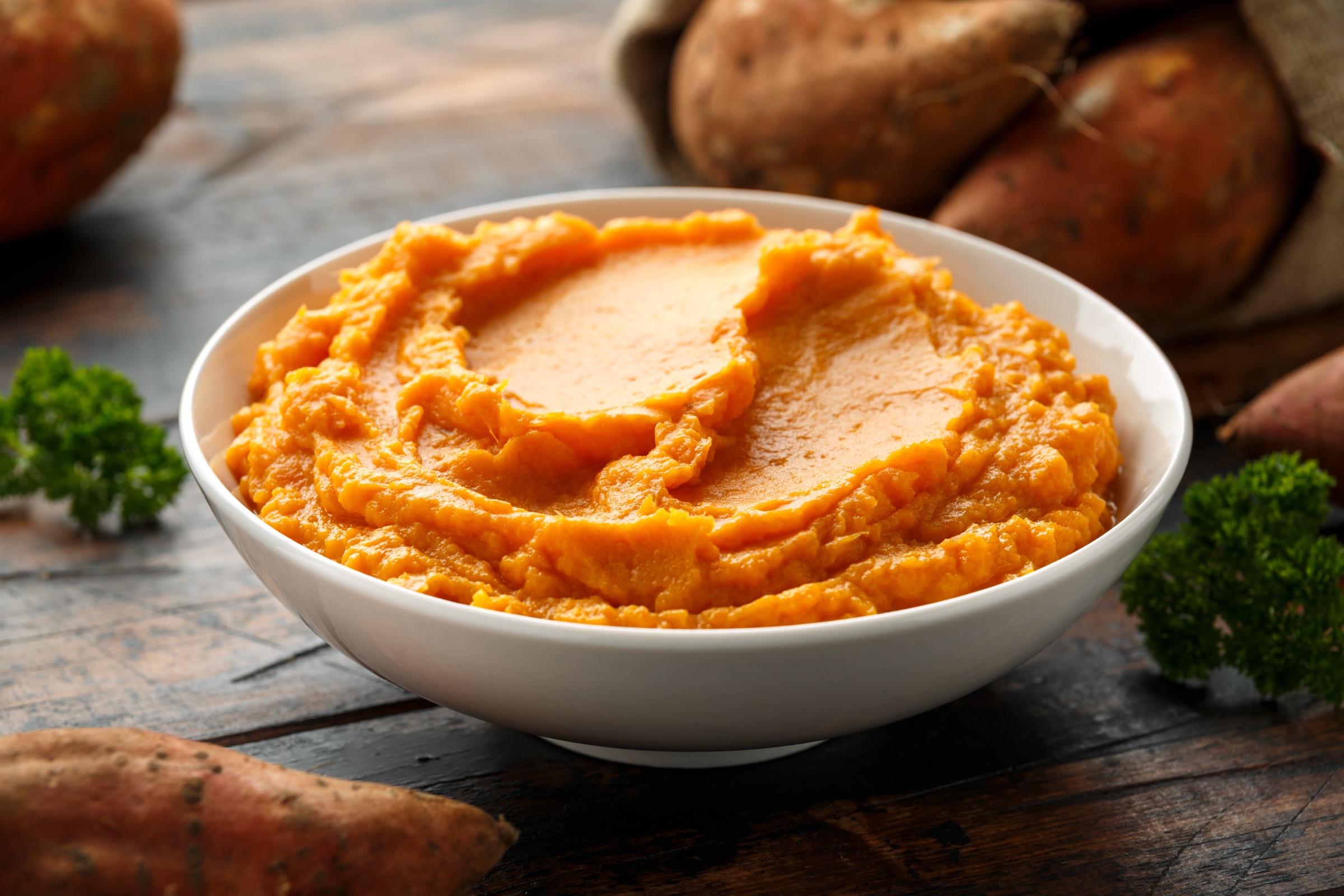 Bowl of mashed sweet potatoes with whole sweet potatoes on a wooden table